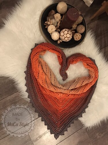 Gehäkeltes Dreieckstuch in Orange- und Brauntönen mit Lochmuster und gezacktem Rand, herzförmig auf weißem Fell drapiert, Dekoschale mit Kerze daneben
