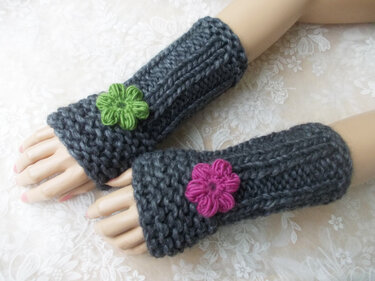 Dunkelgraue gestrickte Armstulpen mit grüner und pinker Blumenapplikation auf Modellhänden