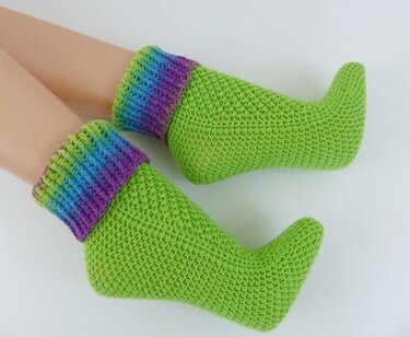 Handgehäkelte leuchtend grüne Socken mit spitzer Zehe und regenbogenfarbenem, geripptem Bündchen auf weißem Hintergrund