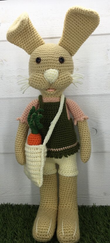 Gehäkelter beiger Amigurumi-Hase mit grünem Latzkleid und Umhängetasche mit Möhre