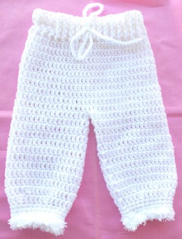 Weiße gehäkelte Babyhose mit Bindeband auf rosa Hintergrund