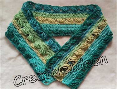 Handgehäkelter Schal mit Streifen in Türkis, Grün und Beige auf hellem Hintergrund.