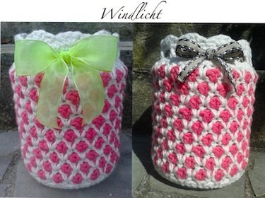 Zwei gehäkelte Windlichthüllen in Rosa und Weiß mit Schleifen auf Steinuntergrund.