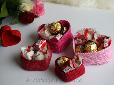 Vier gehäkelte Herzkörbchen in Rot- und Rosatönen, gefüllt mit verpackten Pralinen