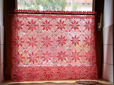 Rote gehäkelte Scheibengardine mit Blumenmotiven vor einem Fensterrahmen