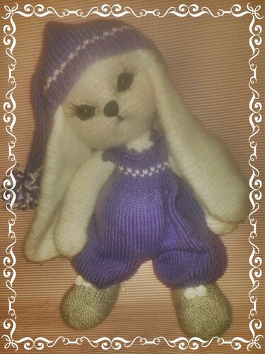 Niedlicher Amigurumi-Schlummerhase mit langen Ohren, lila Mütze und Overall, umrahmt von einem dekorativen Rand.