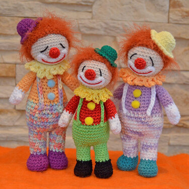 Drei gehäkelte Clowns mit orangefarbenem Haar, bunten Anzügen und kleinen Hüten