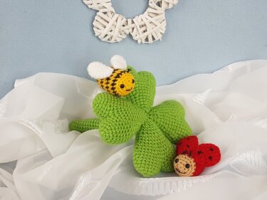Mini-Amigurumi Kleeblatt mit kleiner Biene und Marienkäfer auf hellem Stoff