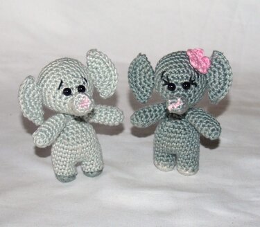 Zwei gehäkelte Amigurumi-Elefanten, hellgrau und dunkelgrau mit rosa Schleife