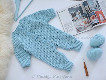 Hellblauer gehäkelter Baby-Strampler mit langen Ärmeln, Rippenbündchen und dreieckigen Knöpfen, neben Garn und Häkelnadel.