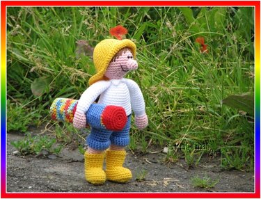 Gehäkelte Amigurumi-Puppe mit gelbem Hut und gerollter bunter Matte im Gras
