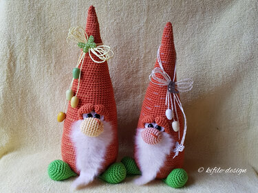 Zwei gehäkelte orange Wichtel mit weißen Bärten, grünen Füßen und Eieranhängern
