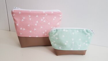 Zwei Kosmetiktaschen in Pastellrosa und Mint mit weißem Dreiecksmuster und braunem Boden, jeweils mit Reißverschluss