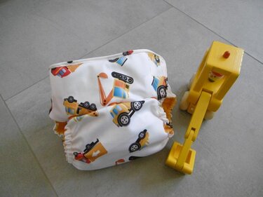 Stoffwindel mit Baustellenfahrzeug-Print und gelbem Holzspielzeugbagger auf grauem Boden
