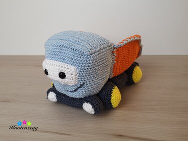 Handmade crocheted amigurumi dump truck in light blue, orange, dark grey and yellow with a smiling face