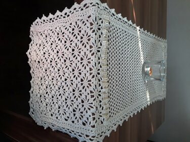 Weißer gehäkelter Tischläufer mit floralen Motiven und Spitzenrand auf dunklem Holz