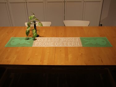 Gehäkelter grüner und weißer Tischläufer mit Fischmotiven auf Holztisch