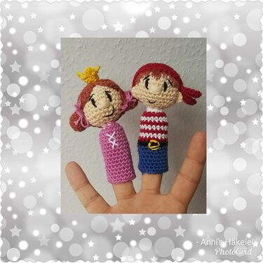 Hand mit zwei gehäkelten Fingerpuppen: Prinzessin mit Krone und Pirat mit gestreiftem Oberteil, vor hellem, leicht strukturiertem Hintergrund.