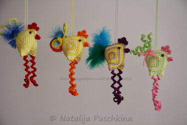 Four hanging crocheted chick ornaments in yellow, orange, purple and green with curly spiral legs and feather tails