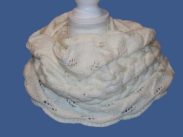 Cremeweißer gestrickter Loop-Schal mit Zopf- und Lochmuster auf einer Schaufensterpuppe.