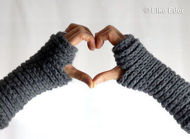 Arms wearing dark grey ribbed crochet wrist warmers forming a heart shape.