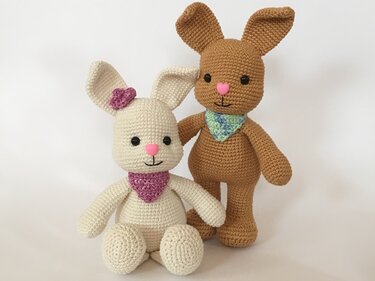 Zwei gehäkelte Amigurumi-Hasen: ein weißer sitzender Hase mit Halstuch sowie ein brauner stehender Hase mit blau-grünem Halstuch