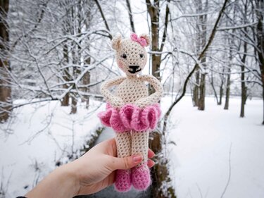 Gehäkelte cremefarbene Ballerina-Maus mit rosa Tutu wird von einer Hand vor verschneitem Hintergrund gehalten