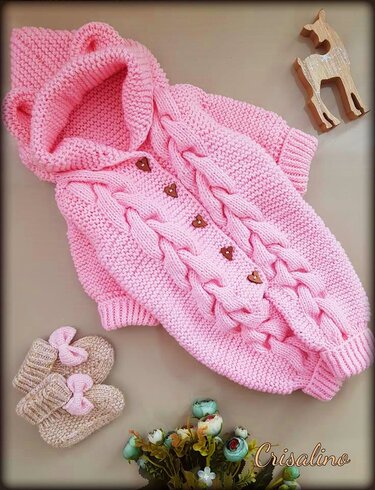 Rosa gestrickter Baby-Overall mit Kapuze, Zopfmuster und herzförmigen Holzknöpfen, dazu beige Strickschühchen