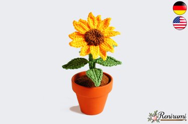 Yellow crocheted sunflower with brown center and green leaves in a terracotta pot on a white background