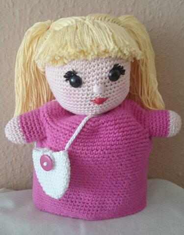 Nahaufnahme einer gehäkelten Handpuppe mit blonden Zöpfen, rosa Kleid und weißer Tasche