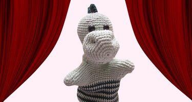 Gehäkelte grün-gestreifte Dino-Handpuppe vor rotem Bühnenvorhang