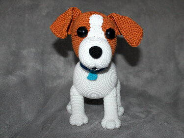 Gehäkeltes Amigurumi-Hundchen, weißer Körper, brauner Kopf, schwarze Augen, blauer Anhänger