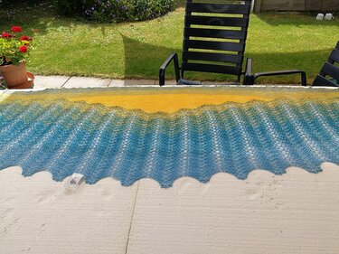 Gestricktes Wellentuch mit Gelb-Blau-Farbverlauf auf Terrasse ausgebreitet