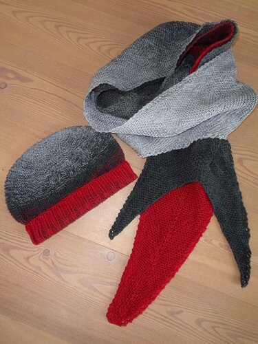 Gestricktes Mützen-Set mit Loop-Schal und Dreieckstuch in Grau und Rot auf Holzboden.