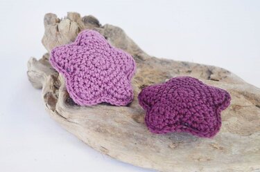 Zwei kleine gehäkelte Sterne in verschiedenen Violetttönen nebeneinander auf Holz