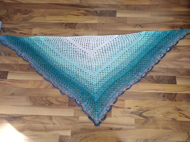 Gehäkeltes Dreieckstuch in Blau‑Türkis‑Farbverlauf mit Lochmuster auf Holzboden