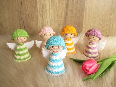 Fünf gehäkelte, gestreifte Engelchen mit weißen Flügeln neben einer Tulpe auf hellem Untergrund