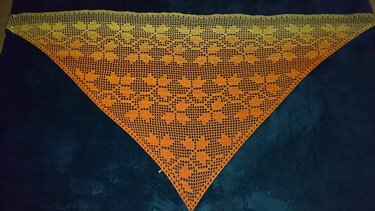 Gehäkeltes Dreieckstuch in Gelb‑Orange mit Herzmuster auf dunklem Untergrund