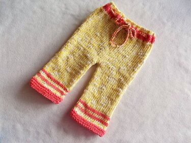 Gestrickte gelb-melierte Kinderhose mit pinken Bündchen und Kordelzug, flach liegend