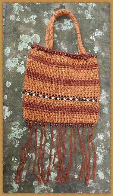 Gehäkelte braune Henkeltasche mit horizontalen Streifen, Holzperlen, schwarz-weißer Perlenborte und langen Fransen.