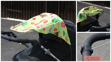 Hellgrüner Kinderwagen-Sonnenschutz mit Hunde- und Blumenmuster, am Griff befestigt.