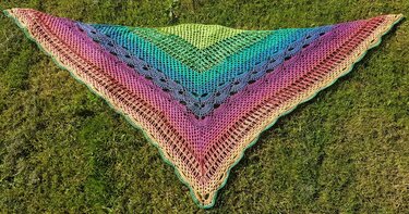 Gehäkeltes Dreieckstuch in Regenbogenfarben mit Netzmuster und Muschelrand auf Rasen