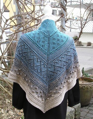 Gestricktes Dreieckstuch mit Farbverlauf in Türkisblau, Grau und Beige, mit Loch- und Noppenmuster auf einer Schneiderpuppe