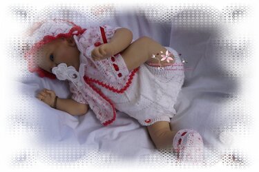 Babypuppe trägt weiß-rotes gestricktes Set mit Mütze, Jäckchen, Strampler und Schühchen