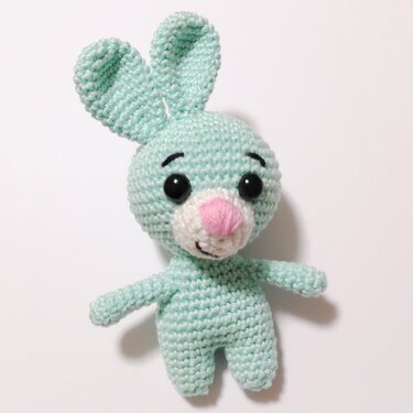 Nahaufnahme eines gehäkelten Amigurumi-Häschens in Mintgrün mit schwarzen Augen und rosa Nase auf weißem Hintergrund.