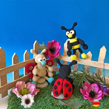 Gehäkelte Amigurumi-Figuren: Marienkäfer, Biene und Schmetterling neben Blumen und Holzzaun