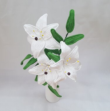 Three white crocheted lily flowers with green leaves in a white vase