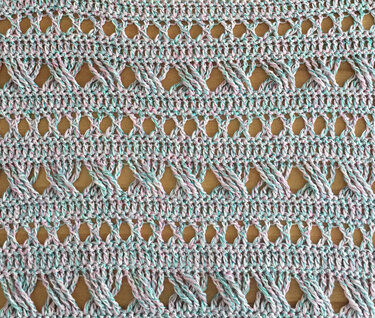 Detail einer Häkelprobe mit überkreuzten Zöpfen und Ajourreihen in pastellfarbenem Garn
