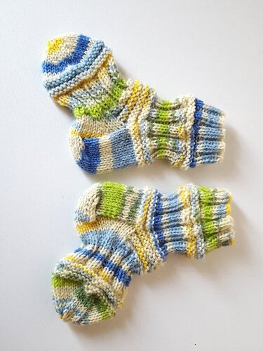 Zwei gestrickte Babysocken mit blauen, grünen und gelben Streifen auf hellem Untergrund