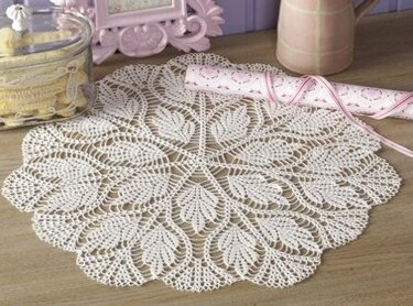 Rundes cremefarbenes Häkeldeckchen mit floralem Spitzenmuster auf Holzfläche